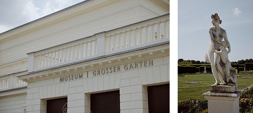 Das Bild zeigt ein weißes Gebäude mit dem Schild „Museum Großer Garten“ auf der linken Seite und einer klassischen Steinstatue einer Frau mit Kind auf der rechten Seite. Diese malerische Szenein den Herrenhäuser Gärten in Hannover, spielt sich vor einer Gartenkulisse unter klarem Himmel ab.