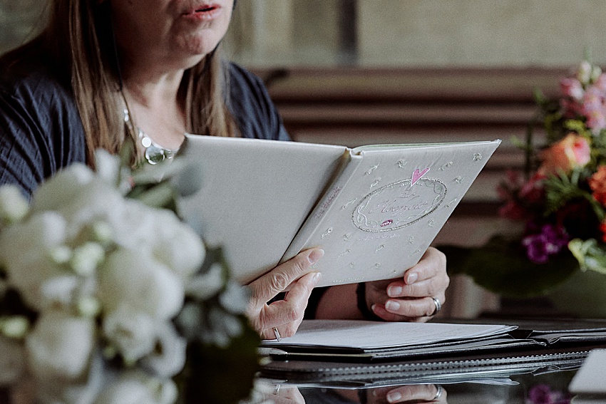 Inmitten der eleganten Blumenarrangements in Weiß und Rosa liest eine Person aus einem dekorativen Buch mit einem Herzmotiv auf dem Einband. Am Tisch mit den Akten sitzend, kann man sich fast vorstellen, wie sie sich auf ihre standesamtliche Hochzeit in Hannovers bezaubernden Herrenhäuser Gärten vorbereitet.