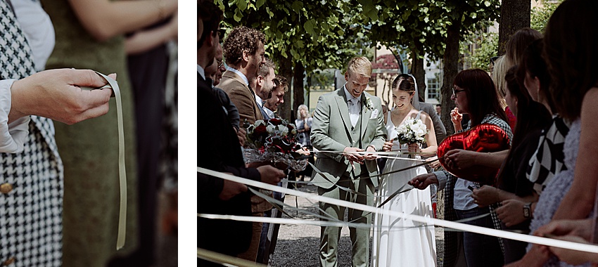 Bei einer standesamtlichen Hochzeit in Hannovers malerischen Herrenhäuser Gärten durchschnitten Braut und Bräutigam unter jubelnden Gästen das Band. Der Bräutigam trägt einen hellgrünen Anzug und die Braut strahlt in ihrem weißen Kleid. Beide strahlen, während sie diesen besonderen Moment im Freien feiern.