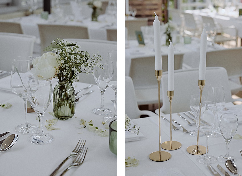 Teilbild einer Hochzeitstafel im charmanten Fischerstübchen Hemmingen. Links: eine grüne Glasvase mit weißen Blumen und leeren Weingläsern. Rechts: drei weiße Stabkerzen in goldenen Haltern, umgeben von leeren Gläsern und Besteck auf einer strahlend weißen Tischdecke.