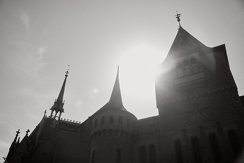 Dieses Schwarzweißbild zeigt Schloss Marienburg, ein historisches Gebäude im gotischen Stil, als Silhouette vor der Sonne. Seine Türme und der zentrale Rundturm zeigen komplizierte architektonische Details. Perfekt für ein Hochzeitsshooting, das Sonnenlicht erzeugt einen atemberaubenden Halo-Effekt.