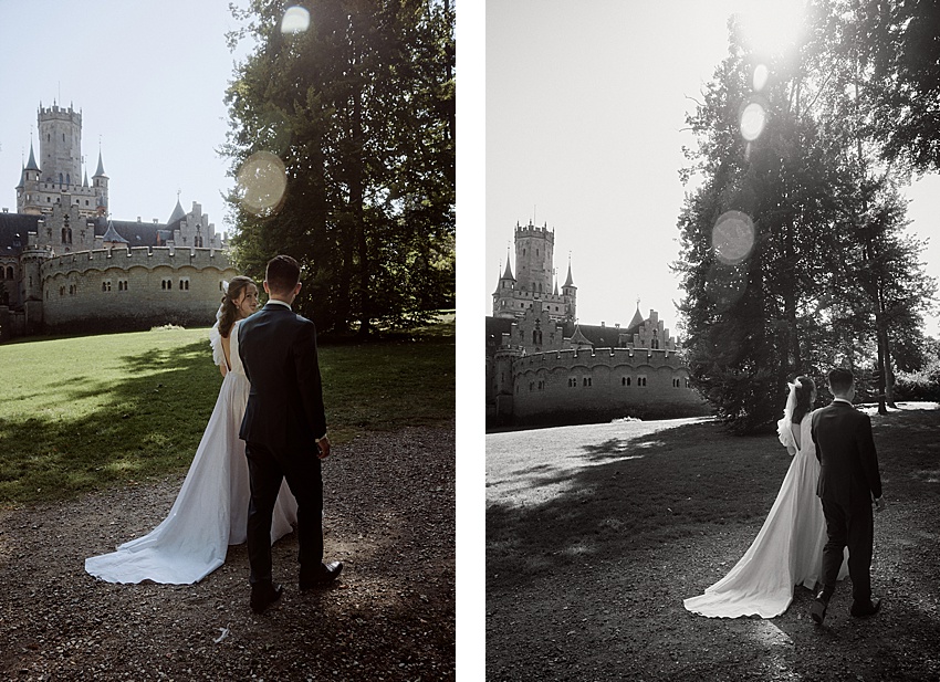 Braut und Bräutigam gehen auf einem Weg zum Schloss Marienburg. Die Szene ist in Schwarzweiß gehalten, Sonnenlicht fällt durch die Bäume. Die Braut trägt ein langes Kleid und der Bräutigam einen Anzug. Dieser historische Ort bietet eine ruhige und malerische Kulisse für ihr Hochzeitsshooting.